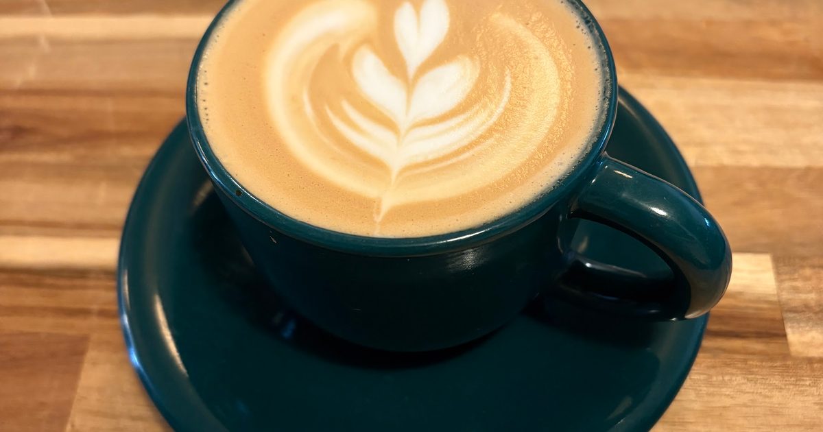 Latte with rosetta art in a teal cup on a wooden table